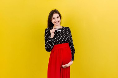 Renkli arka planda mutlu hamile kadın karnına karşı iki şeritli pozitif hamilelik testi. Gri elbiseli müstakbel anne. Hamilelik sürprizi. Boşluğu kopyala.