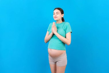 Renkli arka planda dua eden güzel hamile bir kadın..