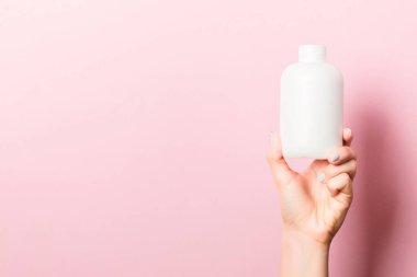 Kadın el tutarak krem şişe losyon izole. Kız pembe arka plan üzerinde tüp kozmetik ürünleri vermek.