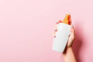 Kadın el losyon izole sprey krem şişe tutarak. Kız pembe arka plan üzerinde kozmetik ürünler vermek.