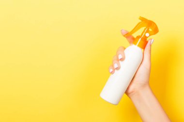 Kadın el losyon izole sprey krem şişe tutarak. Kız sarı arka plan üzerinde kozmetik ürünler vermek.