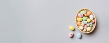 Colorful Easter eggs in wicker basket against colored background, closeup. top view with copy space.