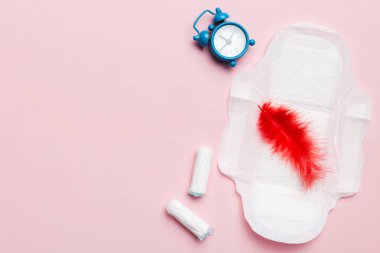 Alarm saatini hijyenik kadın tamponları ve regl pedleri ile çalıyor. Tıbbi konsept kadın kritik günler ve regl dönemi. Kadın günlük hijyen. Boşluğu kopyala.