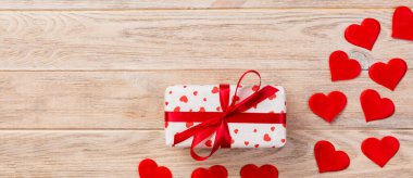 Sevgililer veya diğer tatil el yapımı mevcut kağıt ile tatil sarmalayıcı kırmızı kalpler ve hediye kutusunda. Tasarım için turuncu ahşap masa üstten görünüm kopya alanı ile boş alanı hediye kutusu.