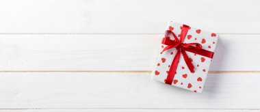 Sevgililer veya diğer tatil el yapımı mevcut kağıt ile tatil sarmalayıcı kırmızı kalpler ve hediye kutusunda. Tasarım için kopya alanı görünümüyle Beyaz ahşap masa üstü, boş alanı kutusu hediye sunmak.