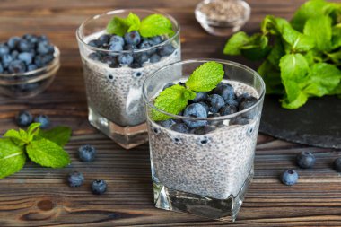 Sağlıklı kahvaltı ve chia tohumlu vanilyalı puding ve böğürtlenli masa arkası, vejetaryen gıda, diyet ve sağlık konsepti. Hindistan cevizi sütü ve yabanmersinli Chia pudingi..