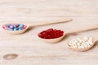 Renkli bir arka planda kaşıkta vitamin kapsülleri. Haplar sağlıklı bir yemek olarak sunuldu. Kırmızı yumuşak jel vitamin takviye kapsülleri kaşık üzerinde.