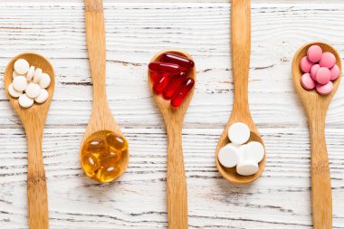 Renkli bir arka planda kaşıkta vitamin kapsülleri. Haplar sağlıklı bir yemek olarak sunuldu. Kırmızı yumuşak jel vitamin takviye kapsülleri kaşık üzerinde.