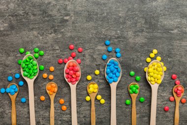 Renkli arka planda kaşık üzerinde renkli tatlı şekerler. Fotokopi alanı ile şekerleme dekoru üst görünümü.