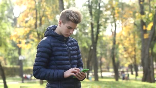 Ung Stilig Kille Blå Jacka Använder Mobiltelefon Höstens Allmänna Park — Stockvideo