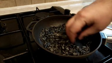 Tavada kızartılmış ayçekirdeği. Adam tavada ayçekirdeği kızartıyor, eliyle karıştırıyor. Yakından bakınca, ay çekirdeği gaz sobasında tavada kızarır..