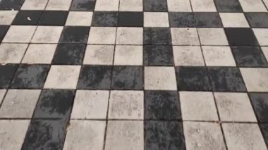 POV, bir şehir caddesinde siyah beyaz fayans yolu boyunca yürüyor. Taş kaldırımdaki ilk kişinin üst görüntüsü..