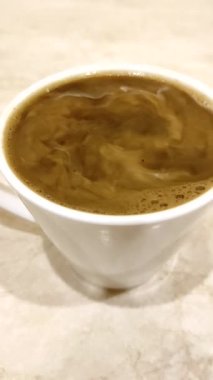 Dikey video, kremalı ya da sütlü bir fincan kahve. Krema kahveye karışıyor..