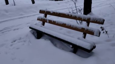 Yoğun kar yağışı sonrası tamamen karla kaplı bir parkta ahşap bir bank. Soğuk kış gününde kar yağışı ve karla kaplı boş bir bank..
