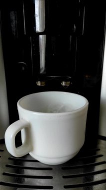 Kahve makinesinde kapuçino yaparken çekilmiş dikey bir video. Kahve makinesinden çırpılmış sütlü beyaz bir fincana dökülen kahve gibi yakın plan. Mocha, kahve zamanı..