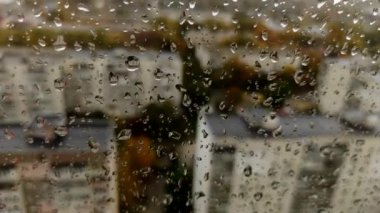 Yağmurdan sonra cam üzerindeki doğal su damlaları. Pencereye su damlıyor, soyut bir arkaplan. Pencerenin dışında yağmur yağıyor. Yağmurlu bir günde şehrin bulanık pencere manzarası.