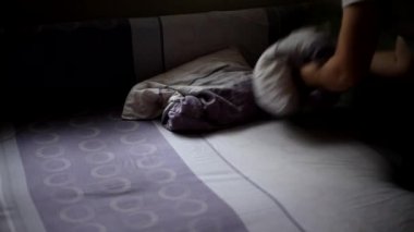 Bir adam bir odada yastık döver ve düzeltir. Uyumak ya da dinlenmek için yatak hazırlıyorum. Ev işi, ev işi ve temizlik konsepti.