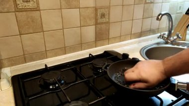 İnsan tavada ayçekirdeğini kızartır ve karıştırır. Yakından çekilen çekirdekler gaz sobasında tavada kızartılır..