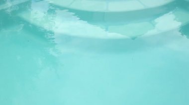 Yüzme havuzunda mavi dalgalı su. Yüzme havuzunda hafif yansımalı su yüzeyi. Suyla dolu bir yüzme havuzunun merdivenlerinin yakın görüntüsü. Rahatlamak ve dinlenmek için şehir havuzu.