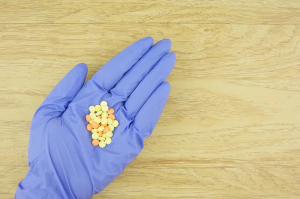Gelbe und orangefarbene Pillen in der Hand tragen lila Latex-Handschuh — Stockfoto