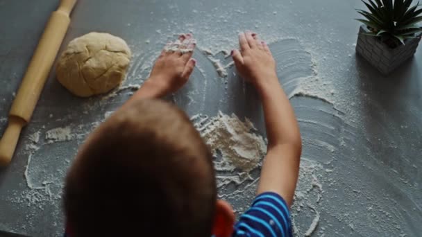 Mały chłopiec niszczy zabawną twarz na stole mąką — Wideo stockowe