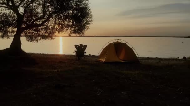 Nehir kıyısında gün batımını izleyen yalnız bir gezgin. Panoramik günbatımı görünümü — Stok video