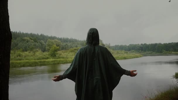 Um homem à chuva na margem do rio. De pé na borda da floresta — Vídeo de Stock