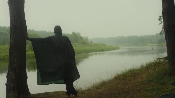 En liten touch av naturen. En man i regnrock på flodstranden. — Stockvideo