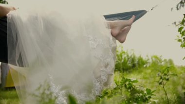 Beyaz gelinlikli gelin nehir kenarındaki hamakta dinleniyor.