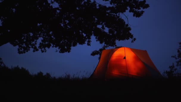 어둠 속에서 빛나고 있는 주황색 천막 안 에는 관광객 이 있다 — 비디오