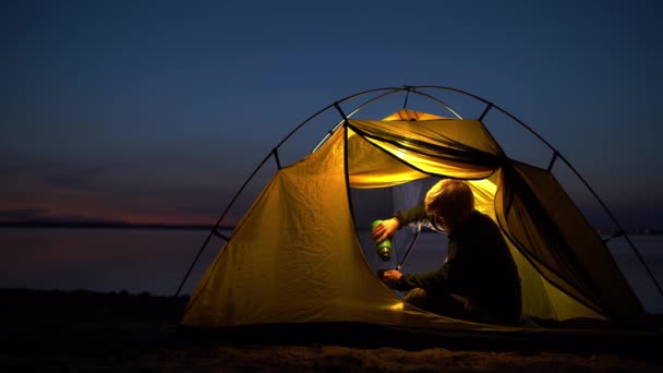 The traveler is sitting comfortably in a yellow tent and pouring a hot drink — Stok video