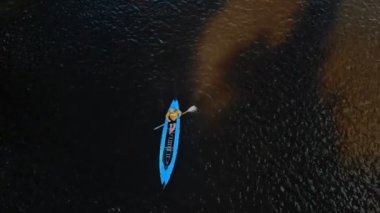 Genç güçlü bir adam mavi bir kanoyla yüzer. Üst görünüm