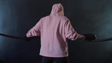 Pembe kapüşonlu bir kız iplere tutunarak ısınıyor.