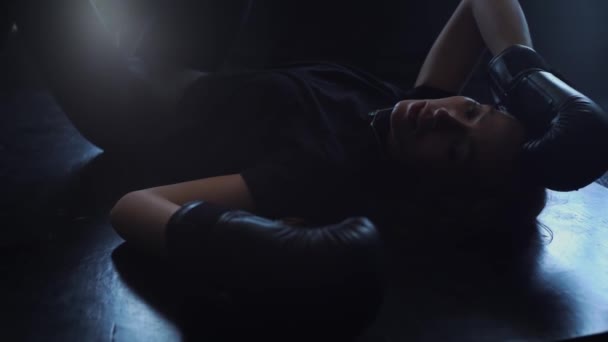 Eine Frau mit Boxhandschuhen liegt nach einem Training erschöpft auf dem Boden — Stockvideo