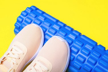 Şeftali rengi spor ayakkabılar ve sarı arka planda masaj silindiri..