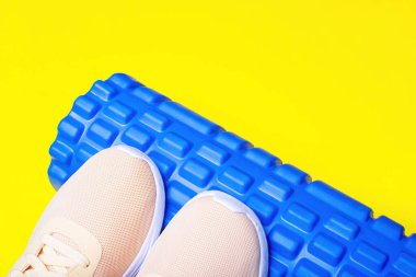 Şeftali rengi spor ayakkabılar ve sarı arka planda masaj silindiri..