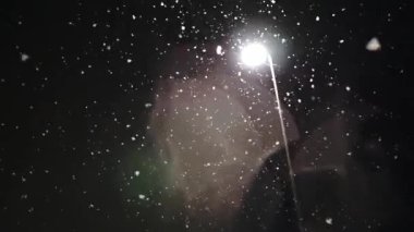 Geceleri parlayan bir fenerin arka planına kar yağıyor.