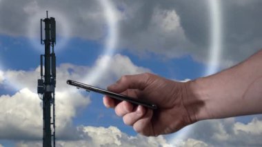 Mavi gökyüzünün önünde 5G Telekomünikasyon Kulesi ve video ile bir iPhone X tutuyor.