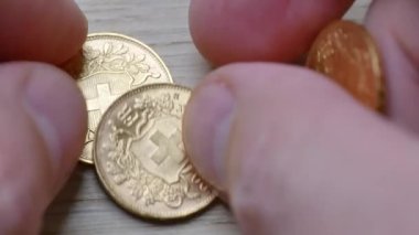 Erkek elleri ahşap bir arka plana 20 İsviçre frangı altın para koyuyor.