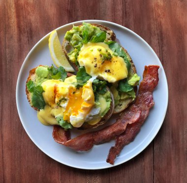 Benedict usulü yumurta. Üst Manzara. Kavrulmuş yumurta ve kızarmış ekmek. Kırılmış avokado, roket, pastırma, Hollandaise sosu ve gri bir tabakta limon..