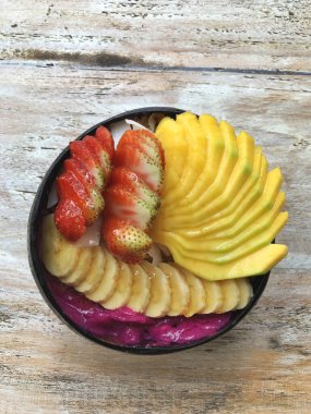 Pitaya kahvaltı kasesi, mango, çilek, muz, ejderha meyvesi, tahıl gevreği ve hindistan cevizi taneli Acai süper yiyecek. Beyaz kırsal ahşap arka plan. Yukarıdan, yukarıdan, dümdüz..