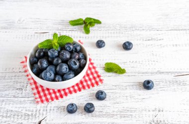 Beyaz ahşap arka planda taze toplanmış yaban mersini kasesi.