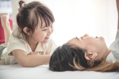 Evde annesiyle yatakta oynayan tatlı küçük bir kız. Covid-19 virüsünden uzakta.