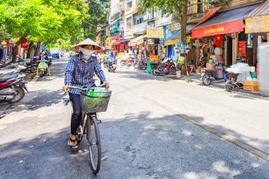 HANOI, VİETNAM 2024 Ağustos: Yerel bir kadının dükkanlardan ve aşırı gelişmiş balkonlardan bisikletle geçtiği kalabalık Hanoi caddesi