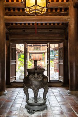 Hanoi 'deki Edebiyat Tapınağı' nın içinde ağır, koyu ahşap sütunlar ve kapılarla dolu açık bir girişe bakan bir iç mekan, atmosferik manzara.