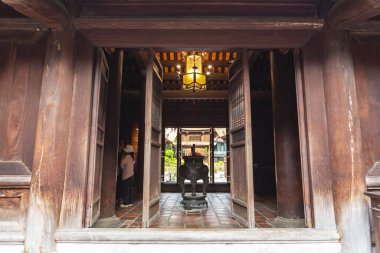 Hanoi 'deki Edebiyat Tapınağı' nın içinde ağır, koyu ahşap sütunlar ve kapılarla dolu açık bir girişe bakan bir iç mekan, atmosferik manzara.