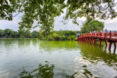 HANOI, VIETNAM 2024, 12 Ağustos: Doğan Güneş Köprüsü olarak bilinen ikonik, geleneksel kırmızı boyanmış ahşap Huc Köprüsü Hanoi 'deki Hoan Kiem Gölü' nün yeşil suları üzerinde uzanır.