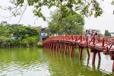 HANOI, VIETNAM 2024, 12 Ağustos: Doğan Güneş Köprüsü olarak bilinen ikonik, geleneksel kırmızı boyanmış ahşap Huc Köprüsü Hanoi 'deki Hoan Kiem Gölü' nün yeşil suları üzerinde uzanır.