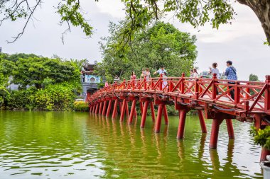 HANOI, VIETNAM 2024, 12 Ağustos: Doğan Güneş Köprüsü olarak bilinen ikonik, geleneksel kırmızı boyanmış ahşap Huc Köprüsü Hanoi 'deki Hoan Kiem Gölü' nün yeşil suları üzerinde uzanır.