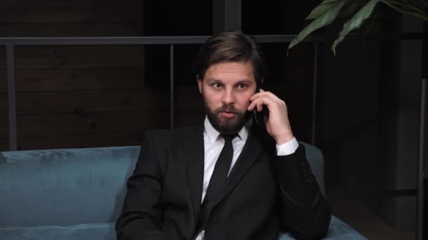 Empresário elegante com barba em um terno clássico está negociando com parceiros por telefone em um prédio de escritórios moderno Negócios. Redes sociais. Gente. Aplicações. — Vídeo de Stock